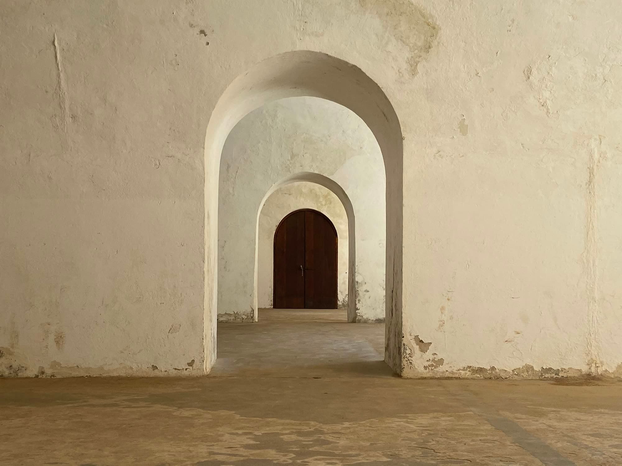 A sequence of whitewashed stone arches receding to a dark timber door.