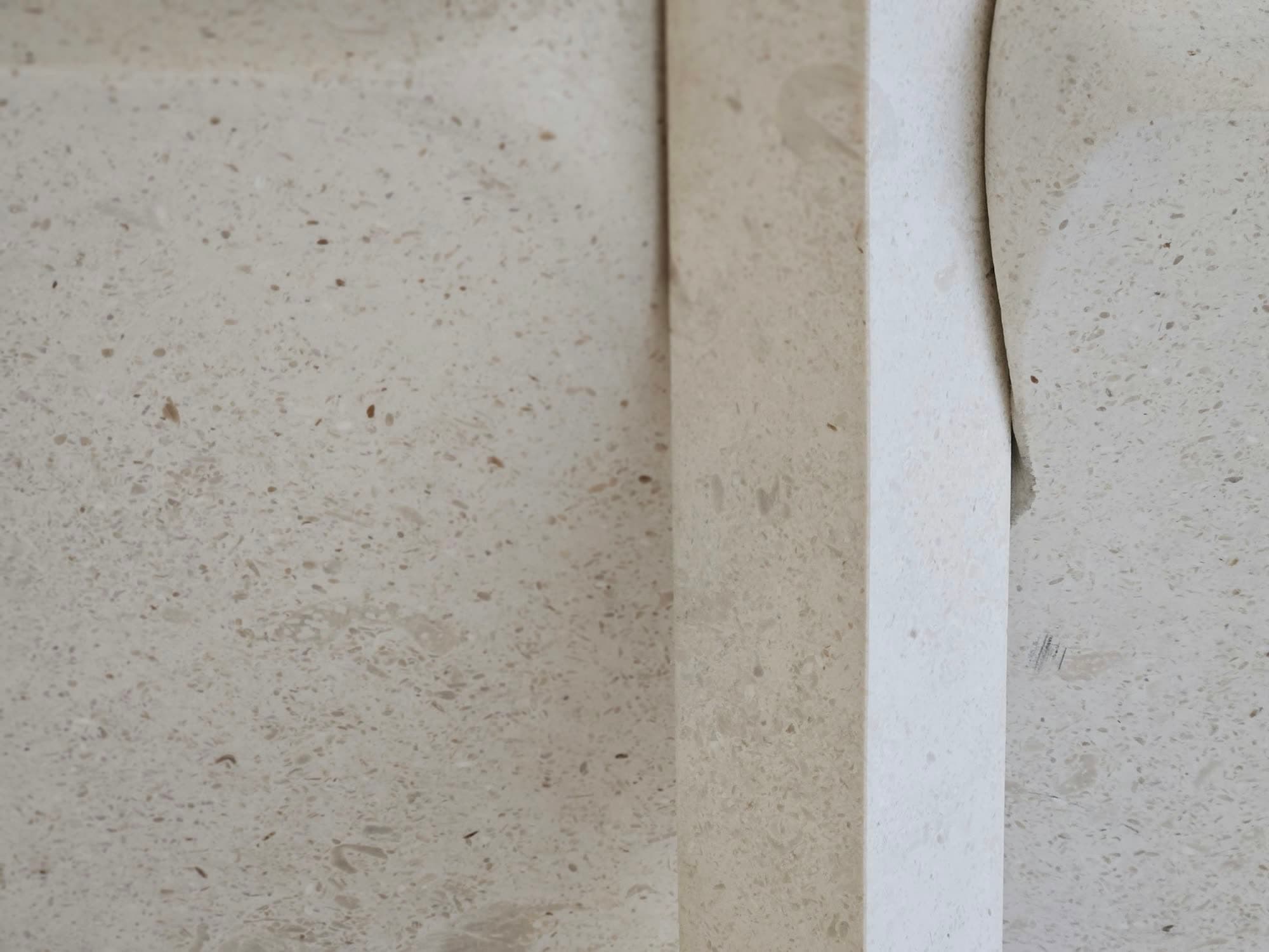 Close detail of pale, pitted limestone meeting a smooth plaster edge.