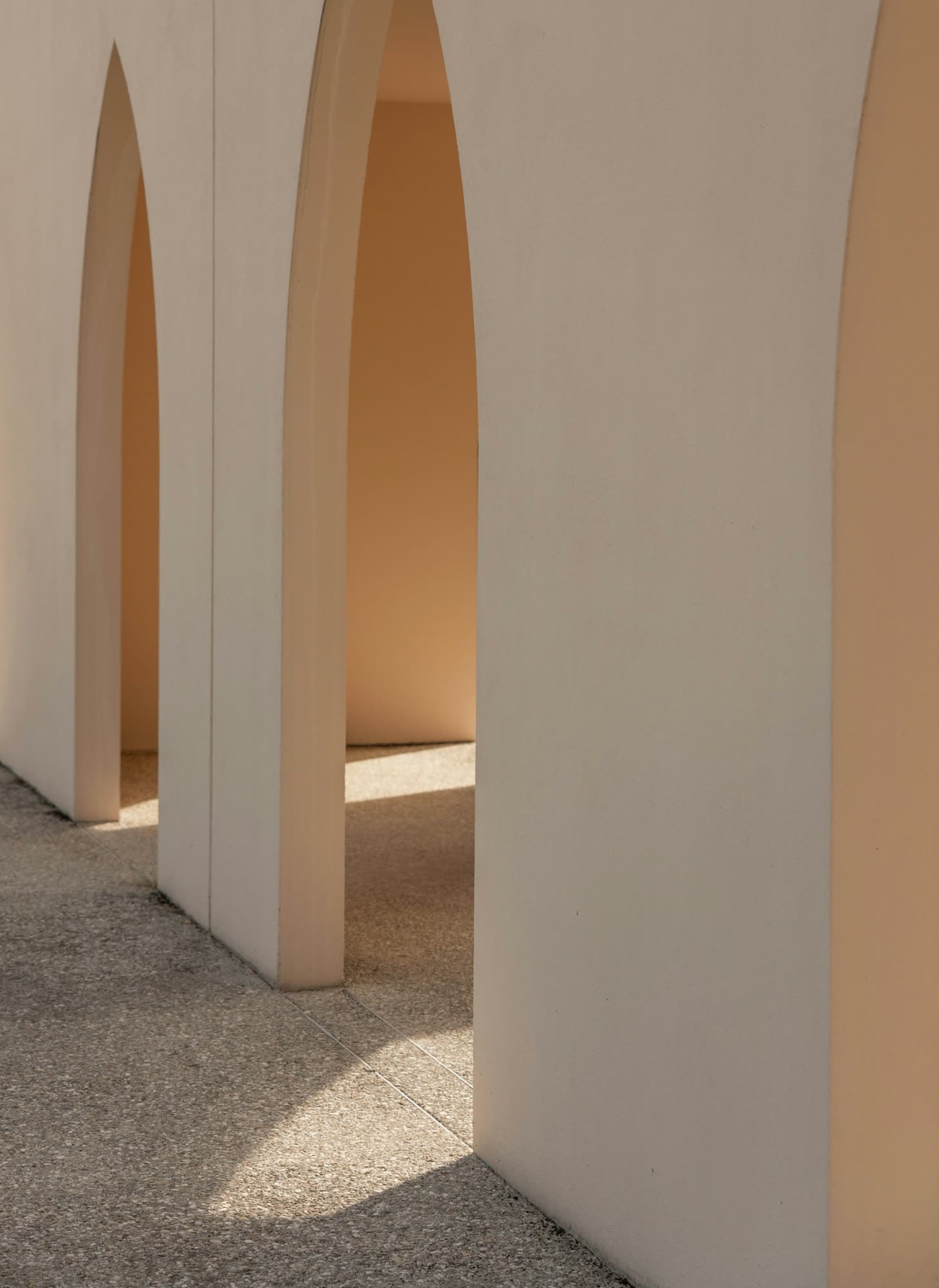 Rounded plaster piers in a quiet colonnade, sun falling across a terrazzo floor.