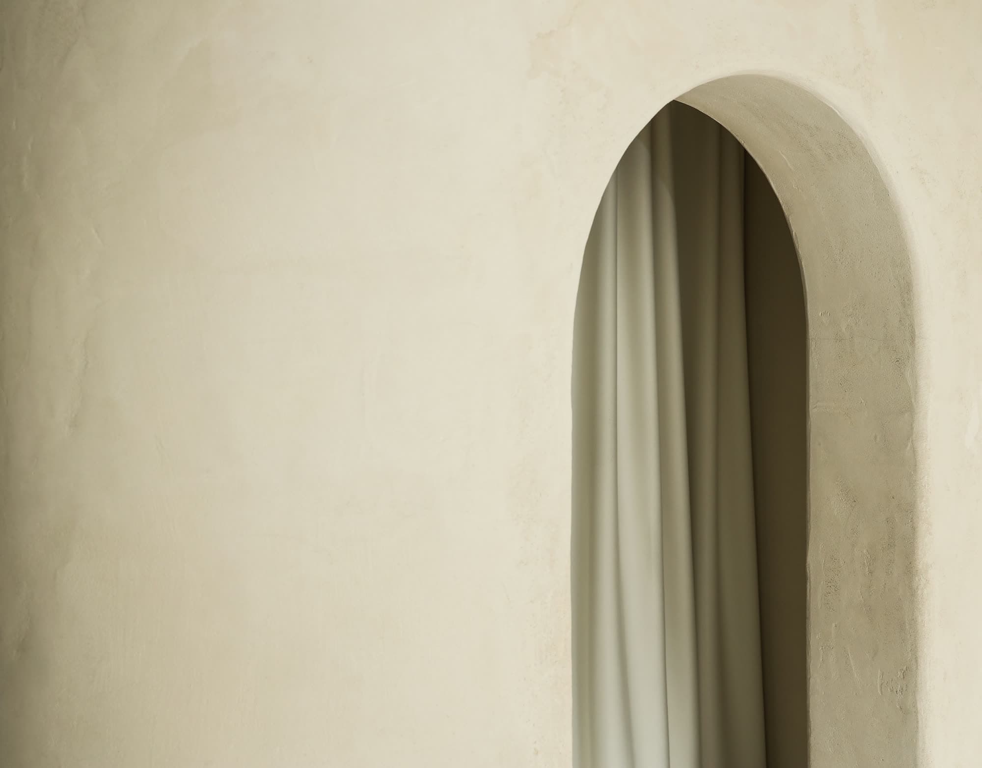 A pale plaster wall with an arched opening, a heavy linen curtain drawn across it.