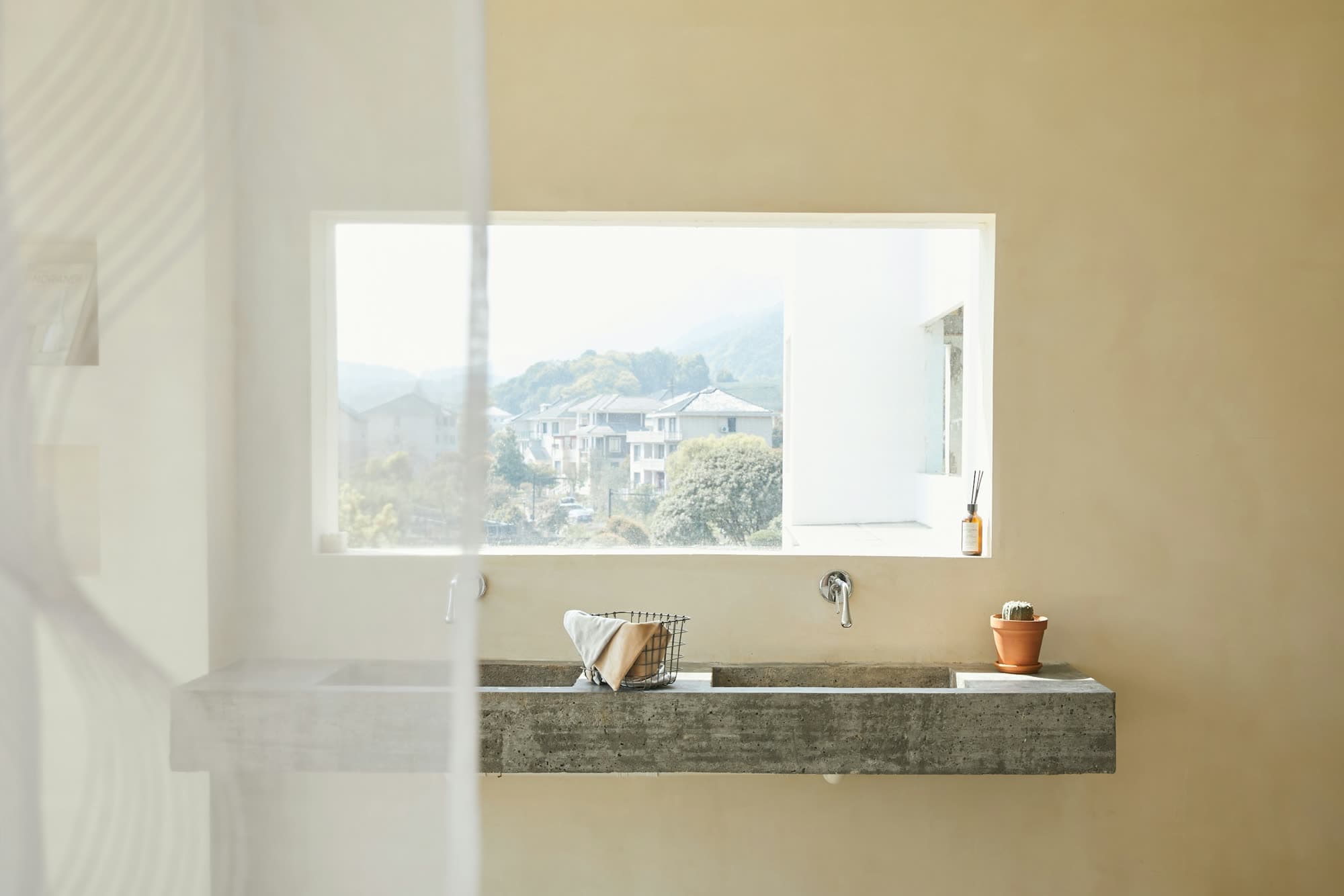 A long stone basin below a wide window, warm plaster walls and hills beyond.