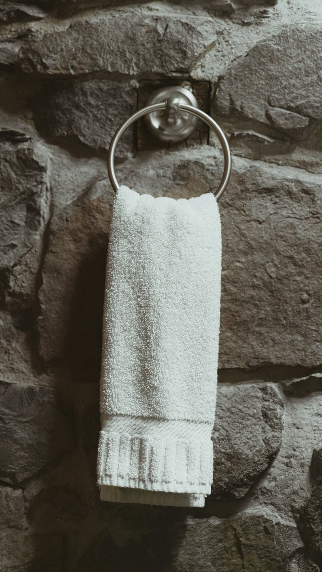 A thick white towel hanging from a ring on a rough stone wall.